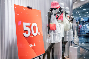 50 percent sale at the window of a fashion store or boutique with clothing options on mannequins....