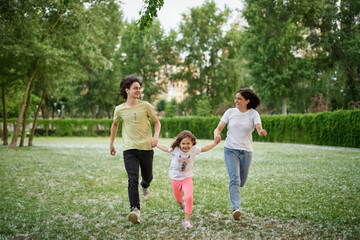 Naklejka na ściany i meble Smiling Family Running Across Summer Field Together. Mother Daughter son, hands together High quality photo