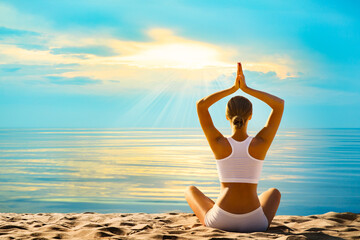 Fototapeta na wymiar Yoga Meditation by Sea. Woman Rear view meditating at Sunset Beach Outdoors. Women Silhouette in Lotus Namaste position over Sunshine Blue Sky background