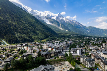 Fototapeta na wymiar Aerial of Chamonix village at the feet of the Mont Blanc Massive mountain range with eternal snow tops in the background during summer. Tourist destination and outdoor winter sports ski resort.