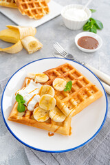 Waffles with banana, whipped cream and salty caramel on a gray concrete background.