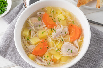 Chicken soup with noodles and vegetables in white bowl on a wooden background.