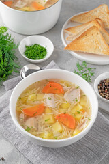 Chicken soup with noodles and vegetables in white bowl on a gray concrete background.