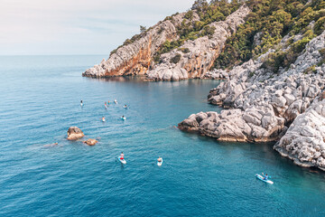 Aerial view of a group or team with paddles swims on a SUP boards on the sea near scenic rocks. Healthy lifestyle and recreation concept