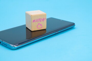 match icon written on wooden cube on mobile phone over blue background.
Concept of romantic relationships on tinder with copy space