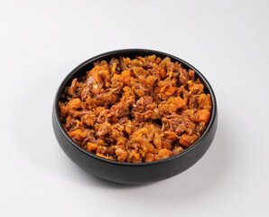 Stewed oxtails with vegetables in a black plate on a white isolated background. Meat stew. The concept of traditional Spanish cuisine.