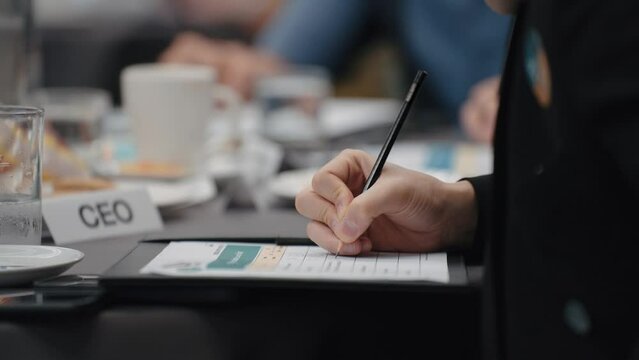 Close up hands of businesswoman taking note at meeting in paperwork on clipboard for meeting minutes. Businesswoman write records at meeting table