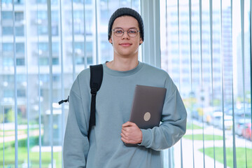 Portrait of college student guy looking at camera holding laptop