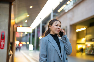 Asian woman using mobile phone during waiting for train at railway station. Attractive girl enjoy urban outdoor lifestyle travel city street with using wireless technology device on holiday vacation.