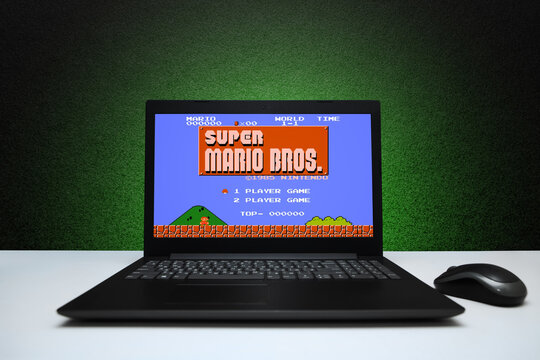 Super Mario Bros classic video game on the screen laptop computer with mouse on black textured wall with green light. Retro game emulator for pc concept. Astana, Kazakhstan - July 3, 2023.