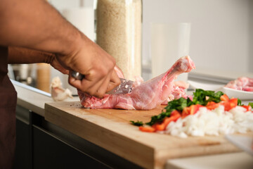 Unrecognizable young black man de-boning chicken to prepare a recipe in a kitchen.