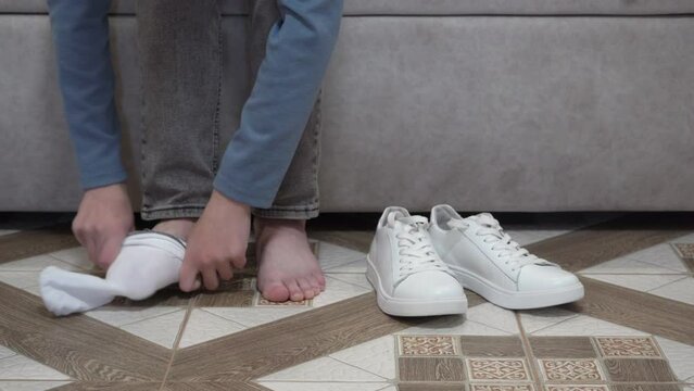 boy put on white socks,the guy gets dressed for a date, the guy on the sofa puts socks on his feet, white sneakers