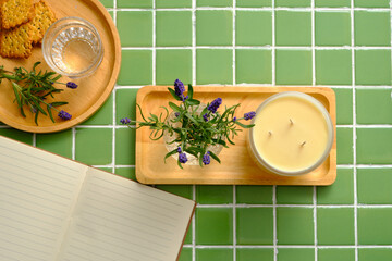 A glass vase of Lavender flowers and scented candle placed on a wooden tray. Wooden tray with a glass of water and some cookies decorated on. Mockup of a book with blank space
