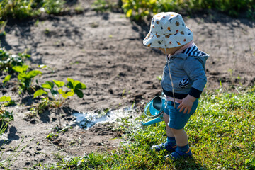 Ein kleiner Junge im Kleinkindalter mit einer Kindergießkanne in einem Garten im Sommer