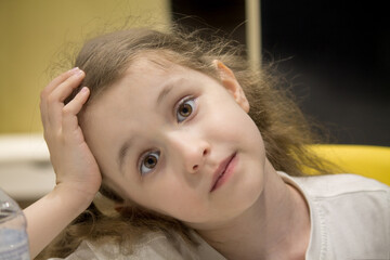 A little girl with brown eyes looks thoughtfully. The concept of childhood, peace and tranquility in a child's gaze