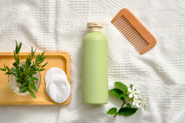 Pastel bottle without label arranged with wooden comb and a tray of green leaves vase and some cotton pads. Cosmetics, products for care and personal hygiene concept