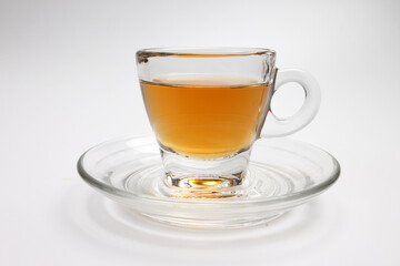 Hot tea in transparent glass cup saucer on white background