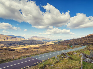 Small asphalt road with stunning nature scenery in county Kerry, Ireland. Amazing Irish landscape by a popular travel rout for tourist. Warm sunny day cloudy sky. Sightseeing and explore wild scenery