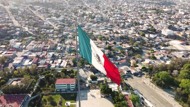 Beautiful aerial shot of Mexican flag waving over the border city of Tijuana. The camera gently pushes in on the flagpole, located dead center in the frame.
