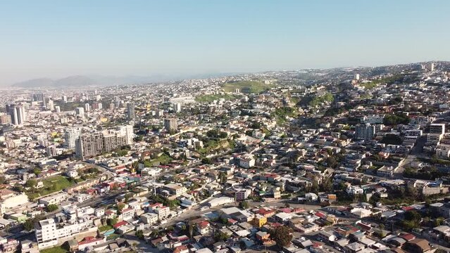 Beautiful aerial shot of the border city of Tijuana. The camera ascends, revealing the sprawling vastness of the city below. The light is soft, close to dusk.