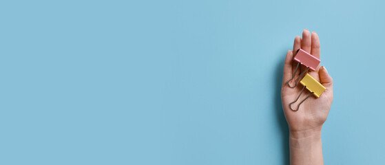 Female hand with binder clips for paper on light blue background with space for text