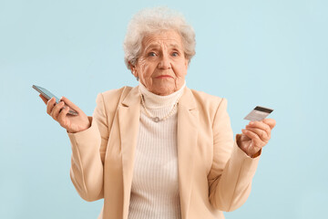 Confused senior woman with mobile phone and credit card on blue background