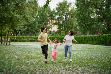 Naklejka na ściany i meble Smiling Family Running Across Summer Field Together. Mother Daughter son, hands together High quality photo