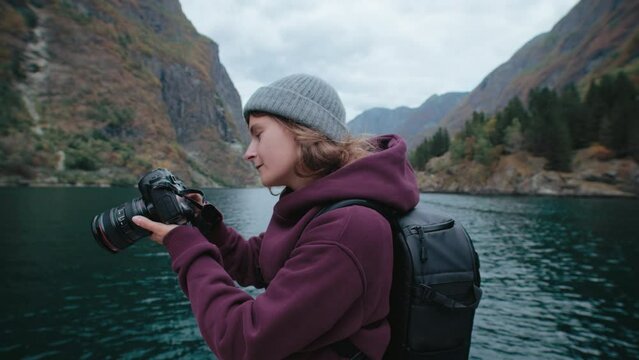 Slow motion portrait of young female content creator photographer hold professional camera with wide angle lens, look straight into camera with proud and empowered look. Woman travel blogger in Norway