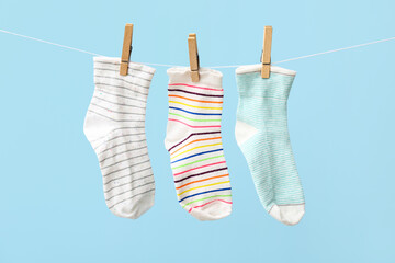 Different socks hanging on rope against color background