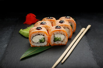 Sushi roll with salmon, on a black background with ginger and wasabi