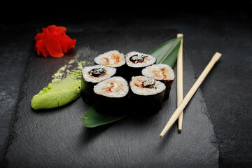 Sushi roll with shrimp and cream cheese, on a black background with ginger and wasabi