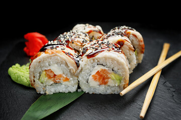 Sushi roll with salmon, cream cheese and avocado, on a black background with ginger and wasabi