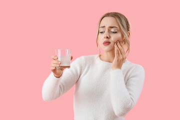 Young woman with dissolved tablet in glass of water suffering from toothache on pink background