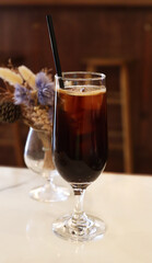 iced americano in the tall glass with flower vase behide on the table