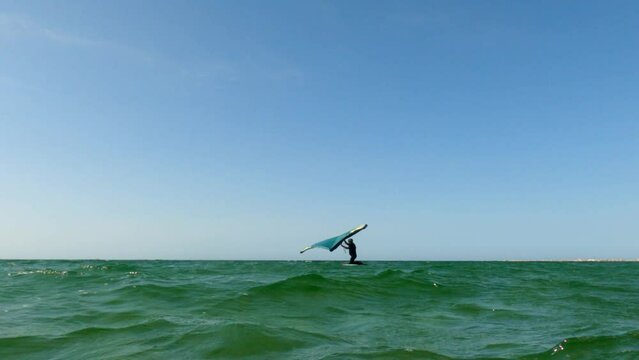 Low angle pov of man on kite board wing surfing on sea surface. Slow-motion sea-level view