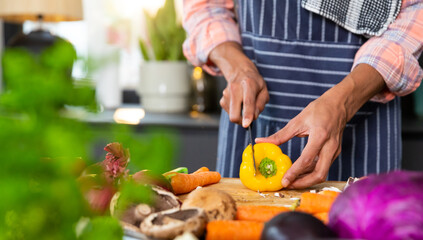 Midsection of biracial man wearing apron preparing meal, chopping vegetables in kitchen, copy space