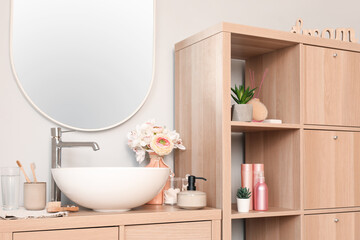 Fototapeta na wymiar Interior of light bathroom with sink bowl, bath accessories and ranunculus flowers