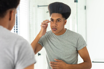 Biracial man looking in mirror inspecting face and eyes in sunny bathroom