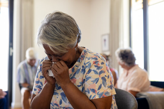 Distressed senior biracial woman holding tissue and crying in group therapy session