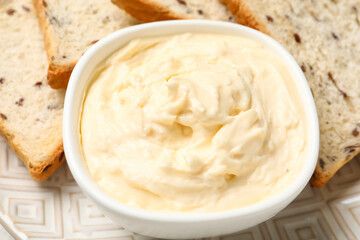 Bowl with tasty cream cheese on plate, closeup