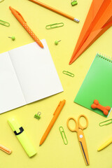 Composition with blank notebook and different school stationery on yellow background