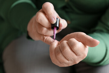 Senior woman applying nail polish at home, closeup