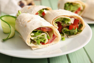 Plate of tasty lavash rolls with tomatoes and greens on green wooden background