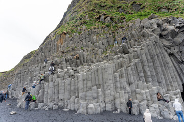 Reynisfjara Black Sand Beach, Iceland - 06.22.2023: People climbing on basalt columns on Reynisfjara beach