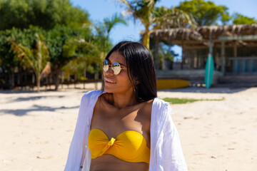 Happy biracial woman wearing sunglasses sitting on sunny beach smiling