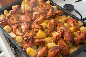Freshly roasted steaming potatoes with chicken wings in metal baking pan