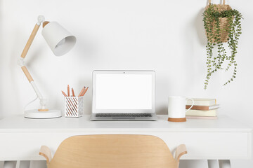 Cozy workspace with laptop, lamp and stationery on wooden desk at home
