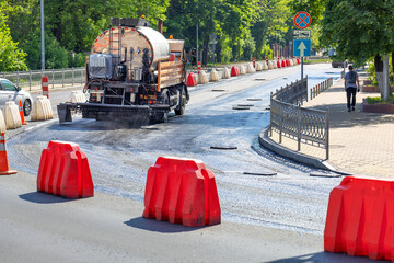 An industrial truck sprays liquid bitumen on a repaired section of a city road before laying new...