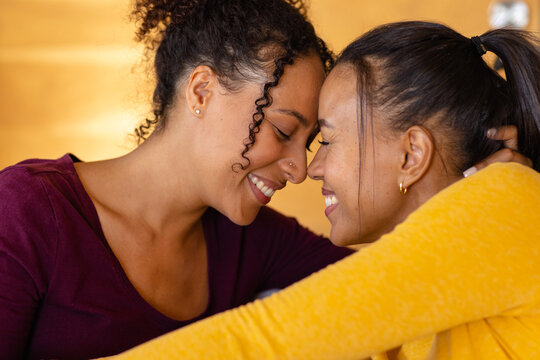Happy biracial lesbian couple embracing and smiling at home