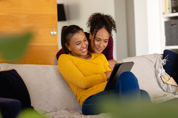 Happy biracial lesbian couple using tablet on sofa in living room